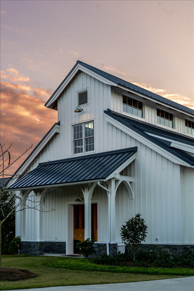 White barn facade with dark metal roof at sunset